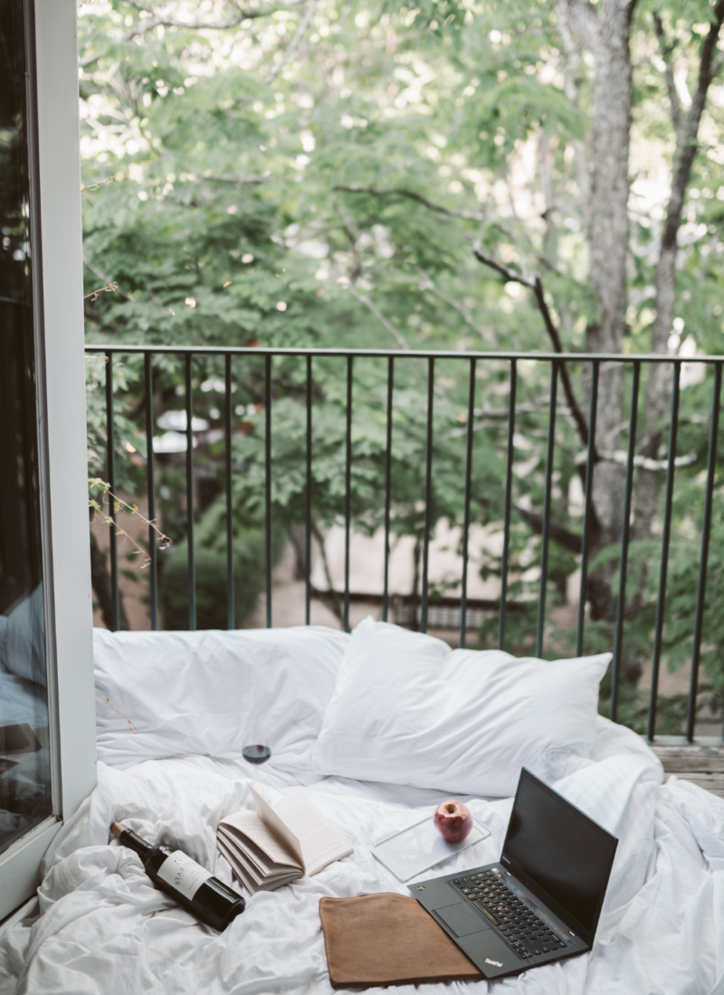 Image of bed beside open balcony door of an Airbnb. A book rests on the bedsheets.