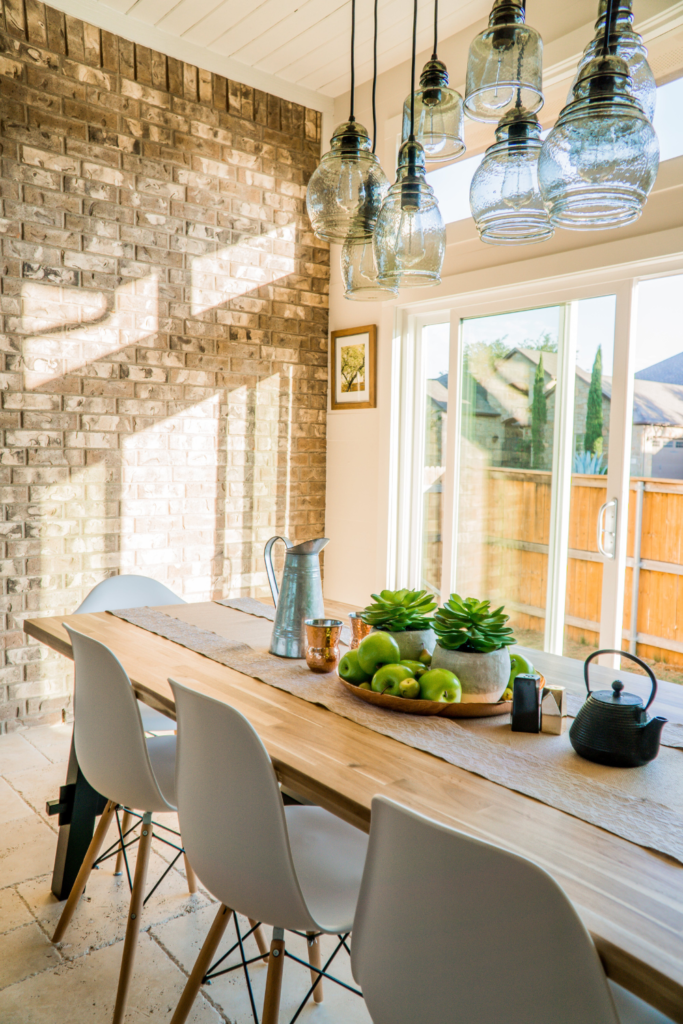 Image of Airbnb dining room. Brightly lit, with wooden table and nice plastic chairs in the center. Beside the table is a tall window letting in sunlight.