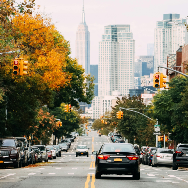 Image of cars on roadway in Atlanta. Trees line both sides of the road, view of Midtown Atlanta up ahead