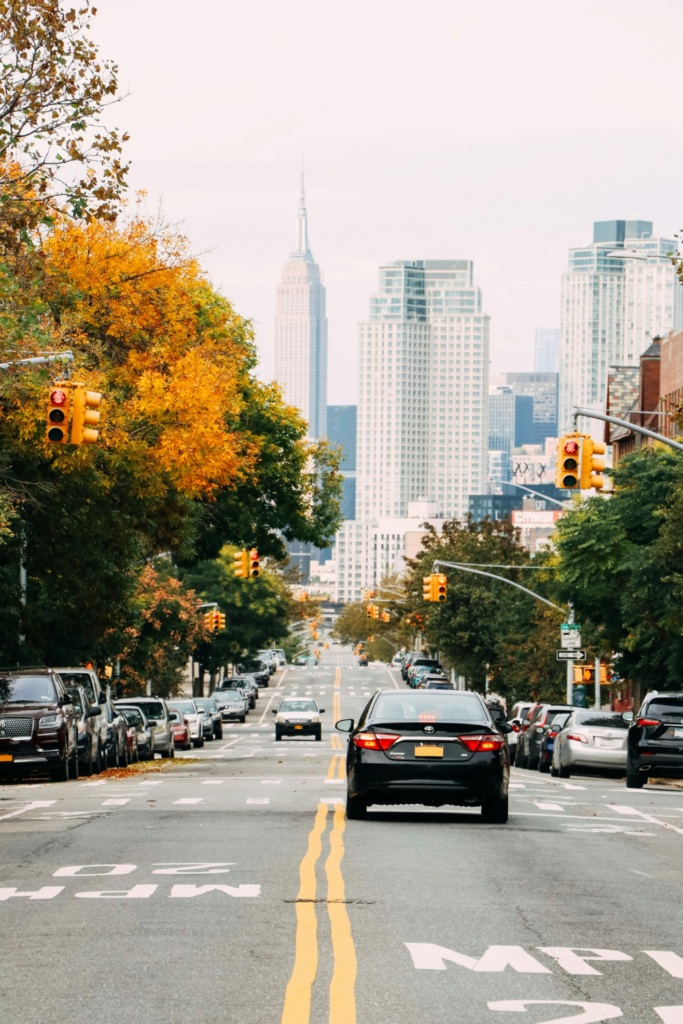 Image of cars on roadway in Atlanta. Trees line both sides of the road, view of Midtown Atlanta up ahead