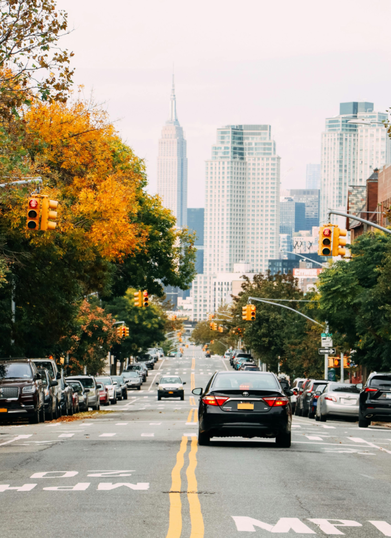 Image of cars on roadway in Atlanta. Trees line both sides of the road, view of Midtown Atlanta up ahead