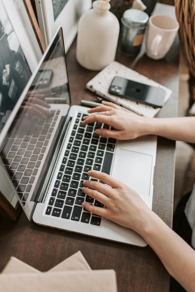 Image of womans hands typing on a laptop checking into Airbnb. Calm setting at desk with natural light