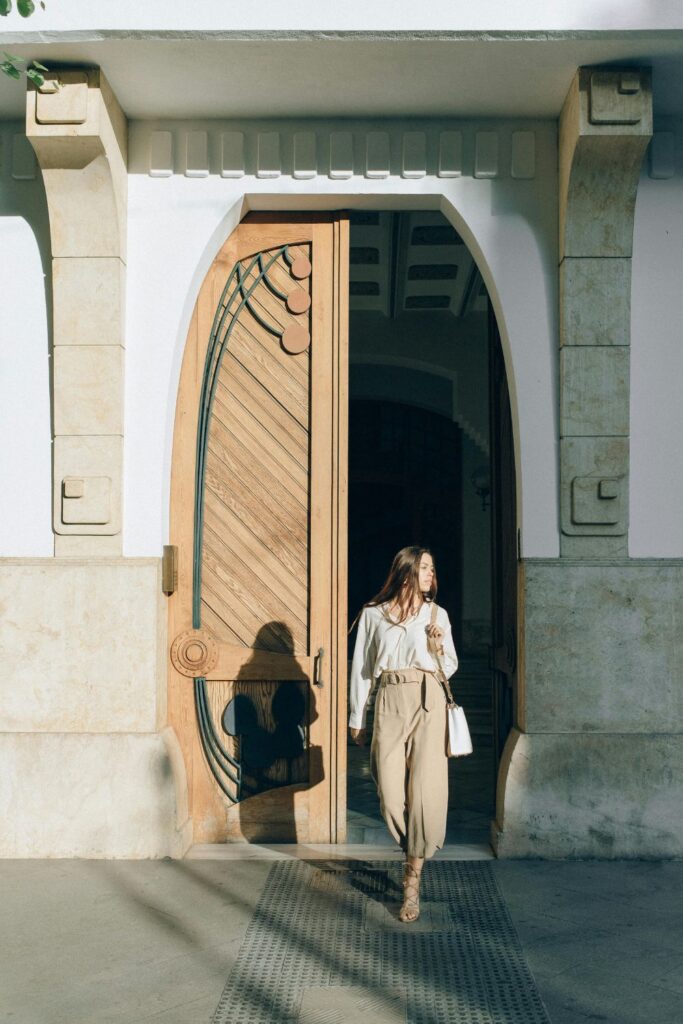 Image of woman in brown top and pants walking out of a large open door, coffee cup in hand