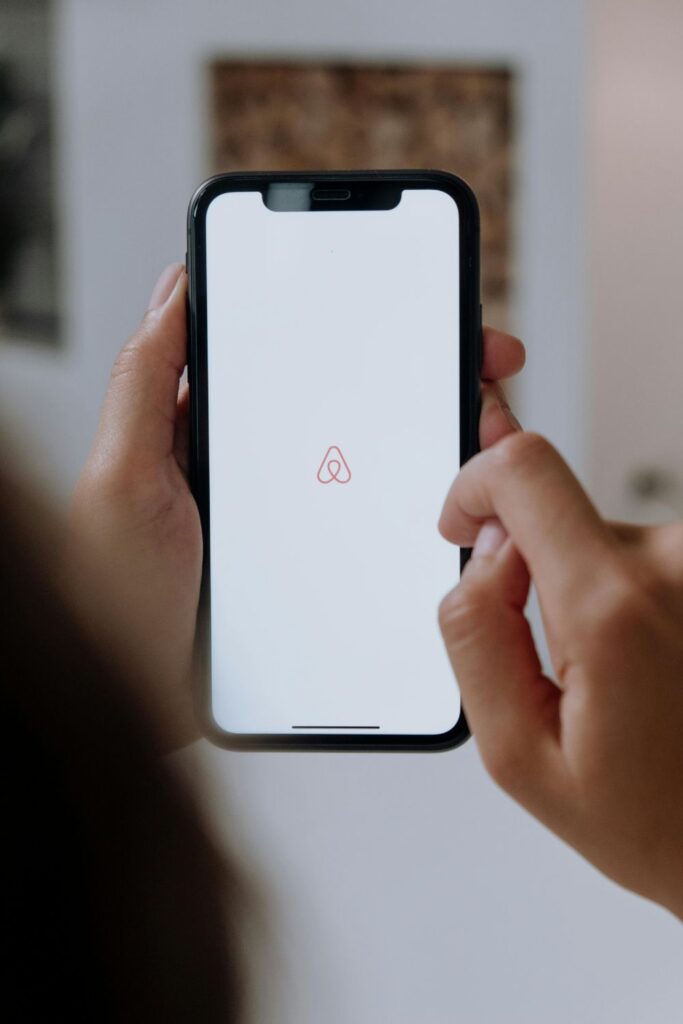 Image of woman's hands holding black cell phone, with Airbnb app opened