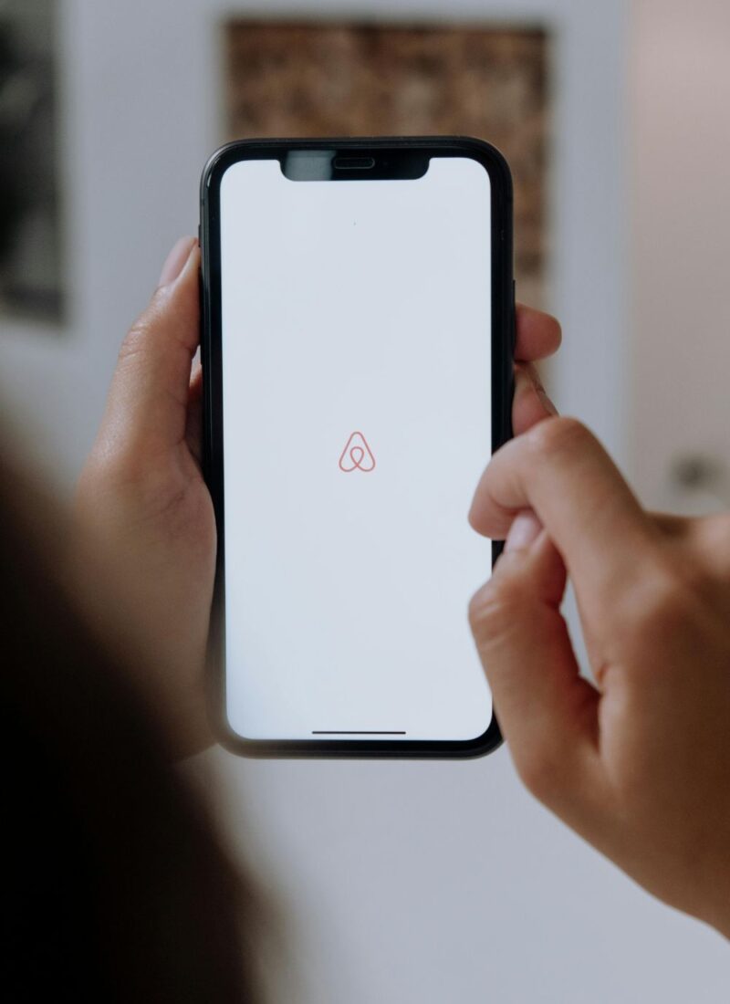 Image of woman's hands holding black cell phone, with Airbnb app opened