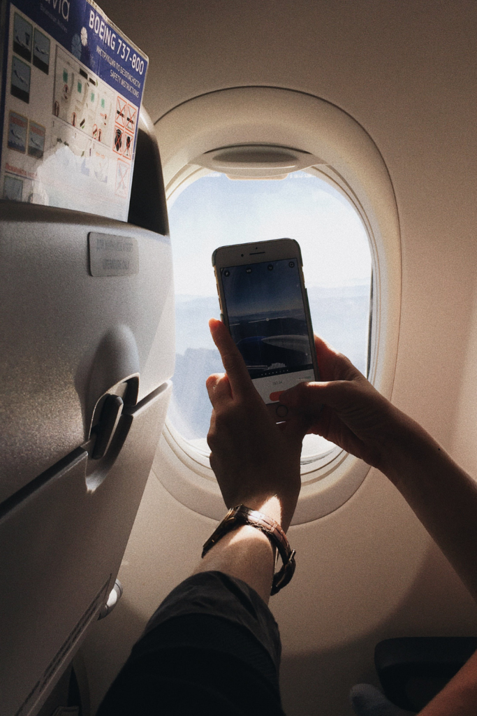 image of someone holding a cell phone up beside an airplane window to take a picture