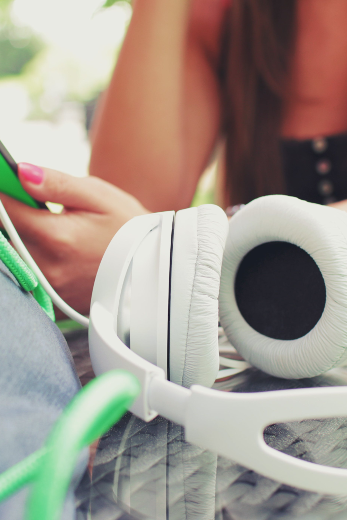 image of white headphones in foreground and hands holding a phone in background