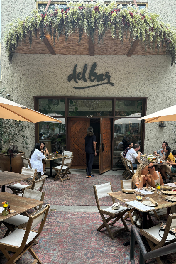 image of exterior of Delbar in Inman Park, Atlanta. Plants, outdoor seating, and persian rugs are shown in the foreground.