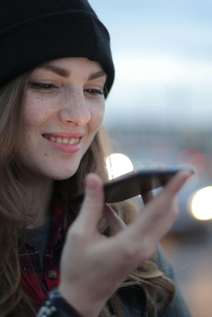 Image of woman with brown hair and black beanie on, holding a smart phone up to her mouth to speak