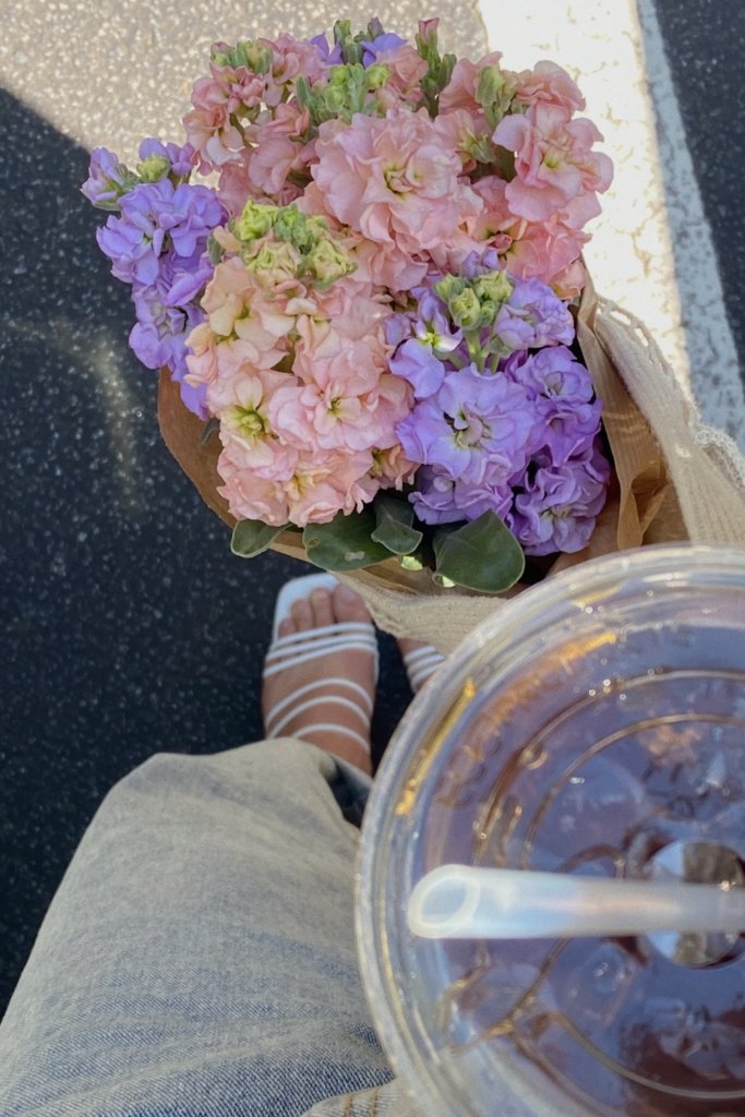 First person point of view looking down at feet walking holding an iced coffee cup and a bouquet of purple and pink flowers in Atlanta Georgia