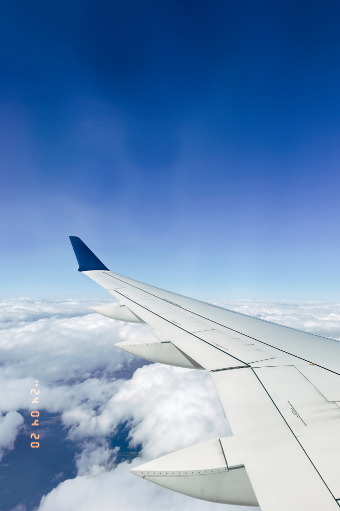 Image looking out of airplane window at a sunny sky with white clouds and an airplane wing on a flight from Atlanta to Hawaii.