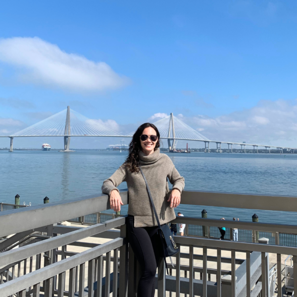 Image of woman smiling and standing in front of the river in Charleston SC against a blue sky