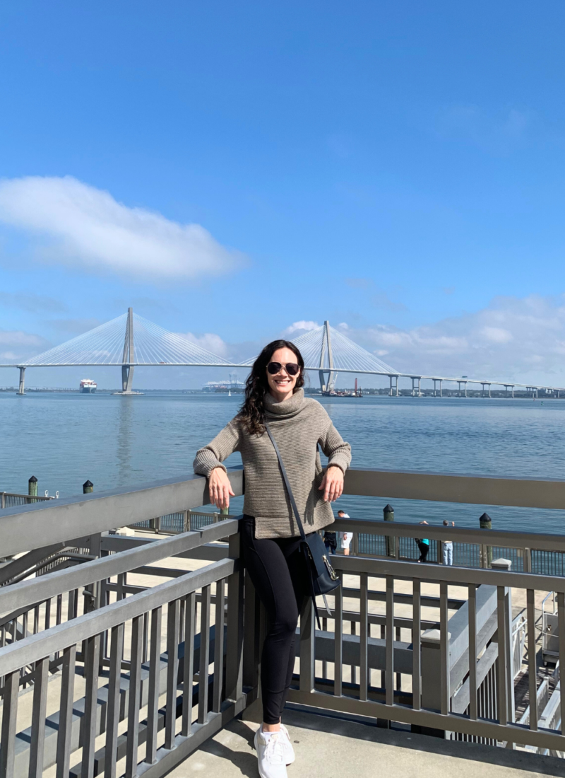 Image of woman smiling and standing in front of the river in Charleston SC against a blue sky