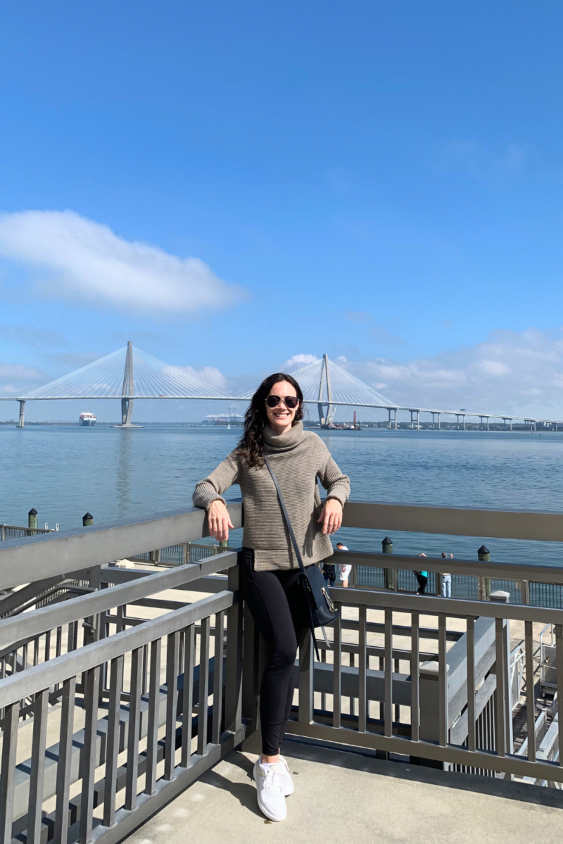 Image of woman smiling and standing in front of the river in Charleston SC against a blue sky