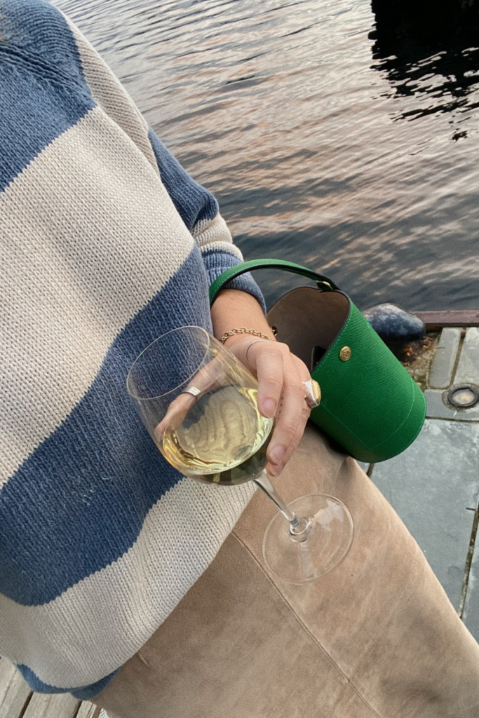 Image of woman with blue and white striped sweater holding a glass of white wine, walking on a dock in Charleston SC for sunset cruise