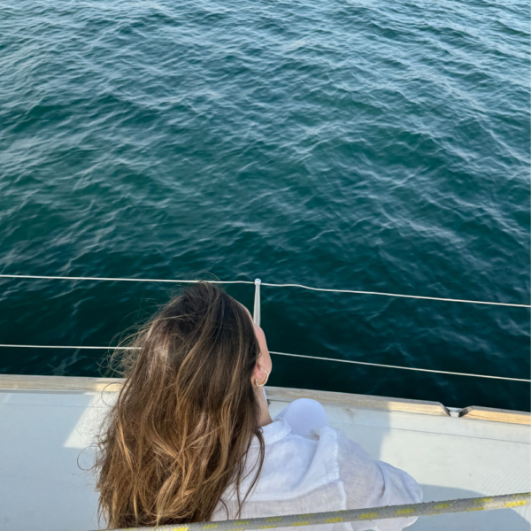 Image of woman with brown hair sitting on the side of a yacht, looking at the ocean during a charleston sc sunset cruise