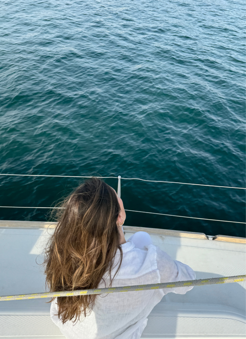 Image of woman with brown hair sitting on the side of a yacht, looking at the ocean during a charleston sc sunset cruise