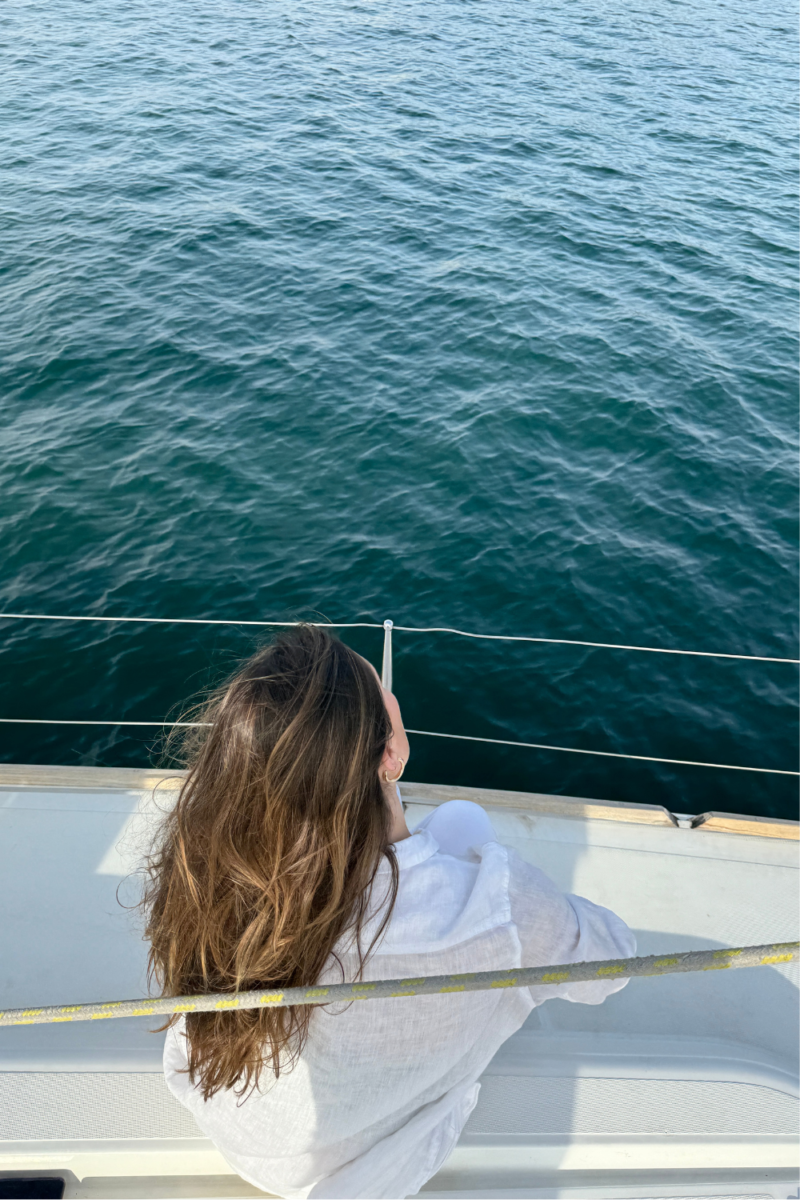 Image of woman with brown hair sitting on the side of a yacht, looking at the ocean during a charleston sc sunset cruise