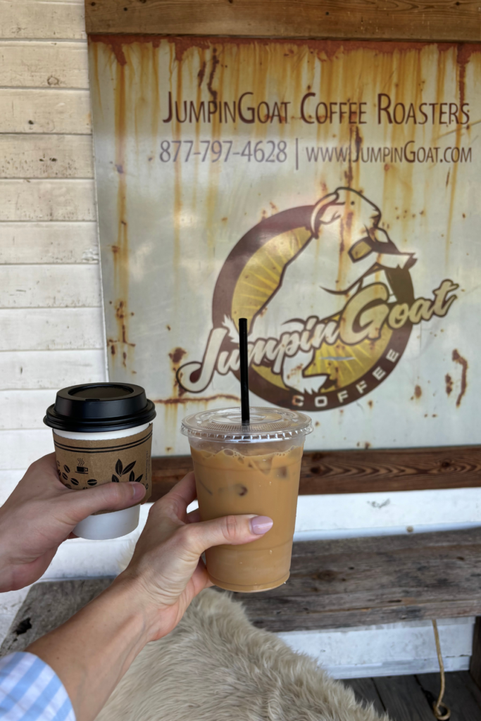 image of 2 hands, one holding ice coffee one holding hot coffee in front of JumpinGoats Coffee Roasters in Helen GA