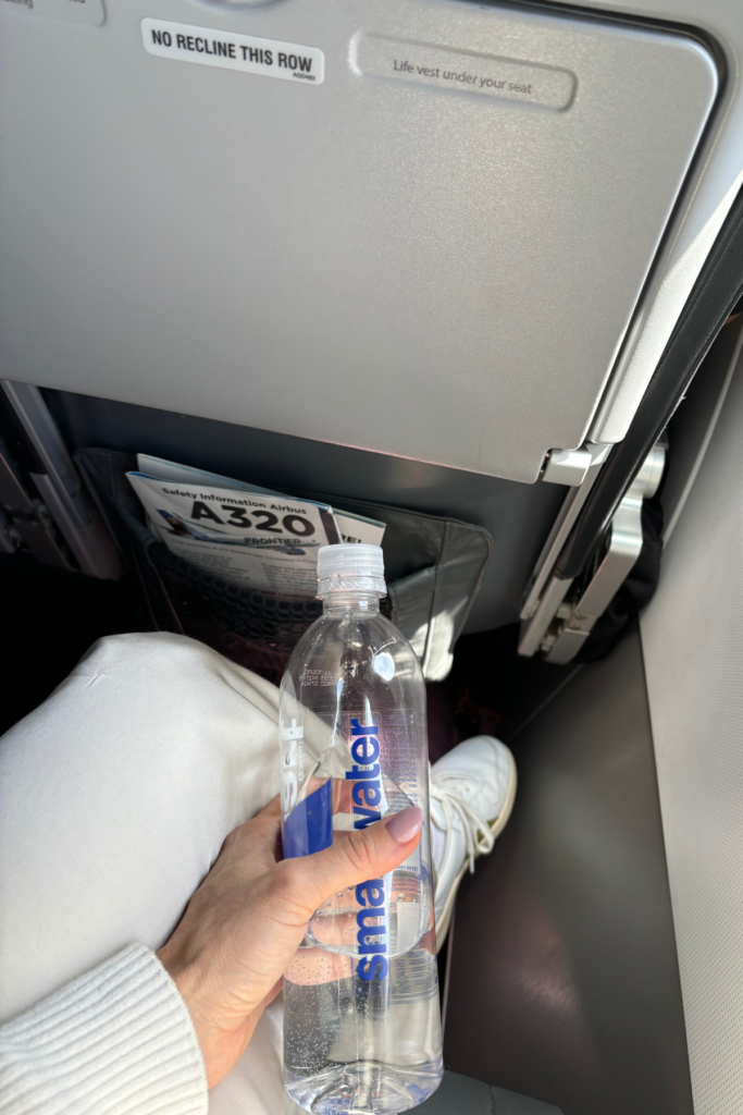 first person point of view of woman sitting in airplane seat holding water bottle and looking at backpack under seat