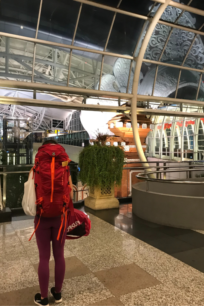 Image of woman and backpack at airport looking into the airport from front entrance