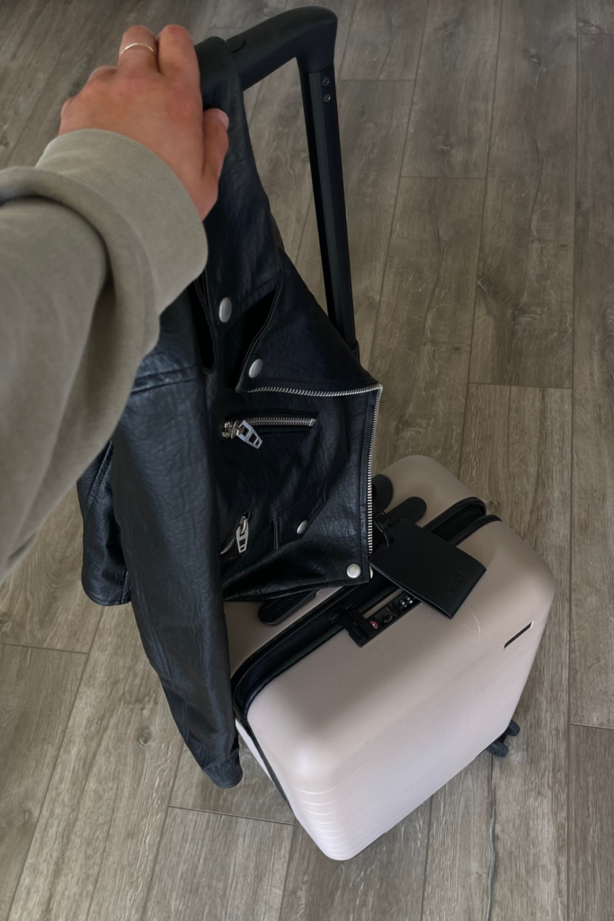 first person point of view looking down at pink carry on suitcase and leather jacket 