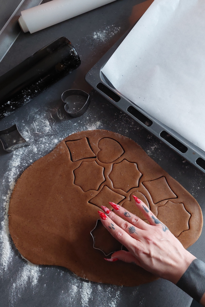 Image of woman's hand with red nails using a cookie cutter to shape Christmas cookies. Part of the 12 tips for how to celebrate Christmas at an Airbnb.