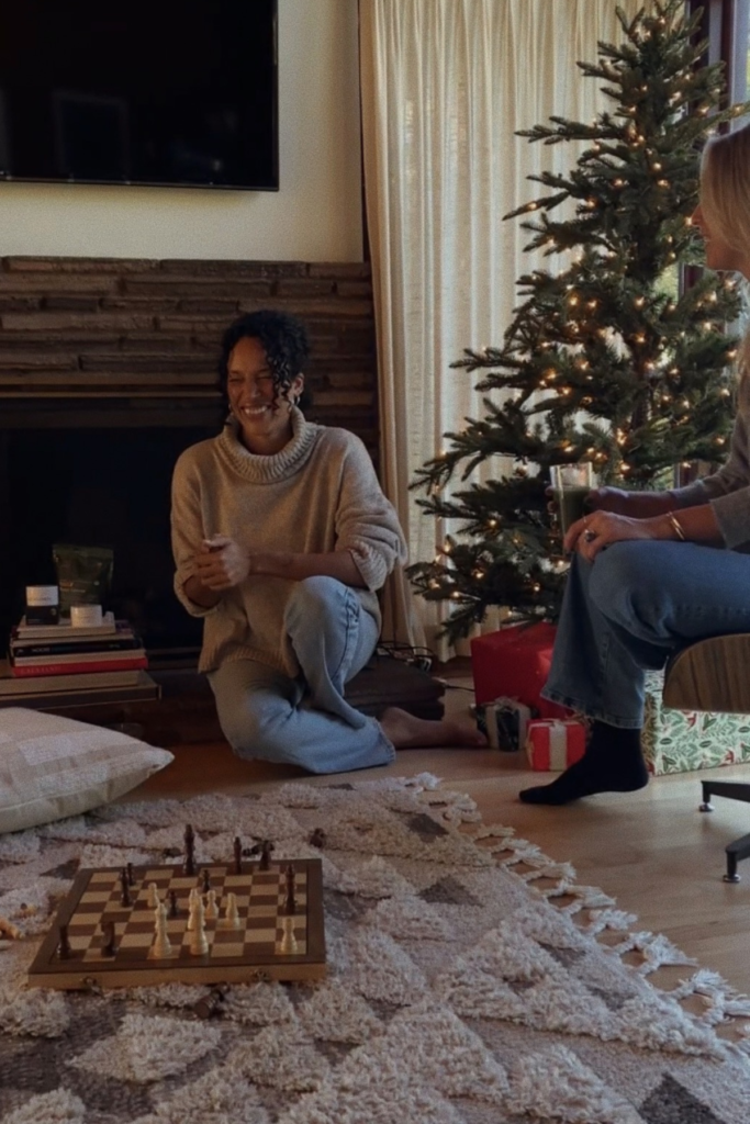 Image of two women sitting in an Airbnb living room beside a Christmas tree playing chess.