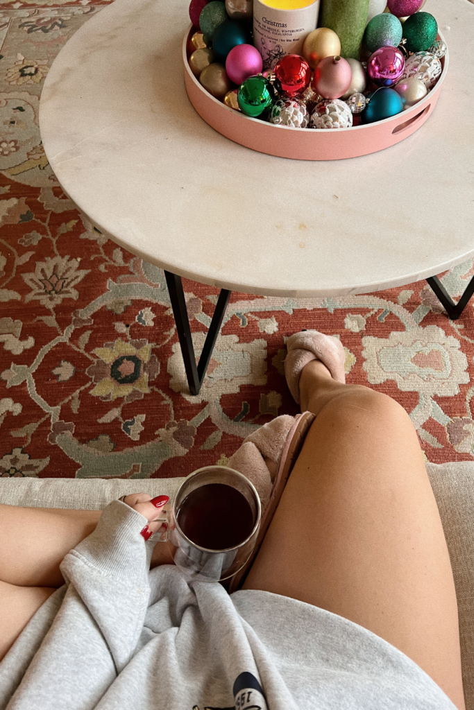 top down image looking at coffee sitting in a woman's lap with coffee table and Christmas decor beside her.