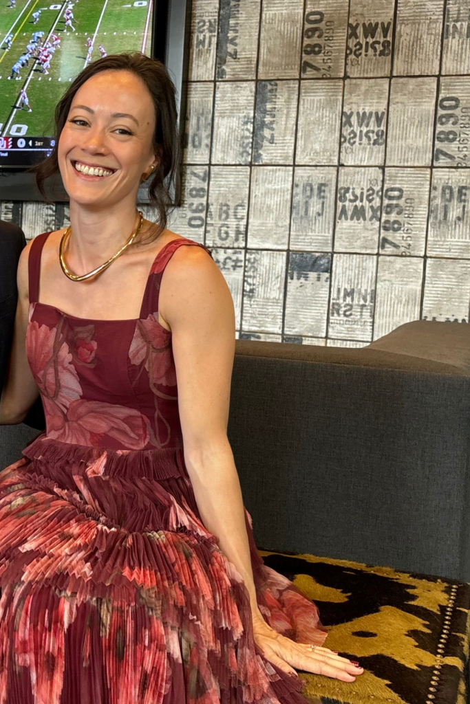 Image of woman in long red dress from Rent the Runway sitting on couch and laughing