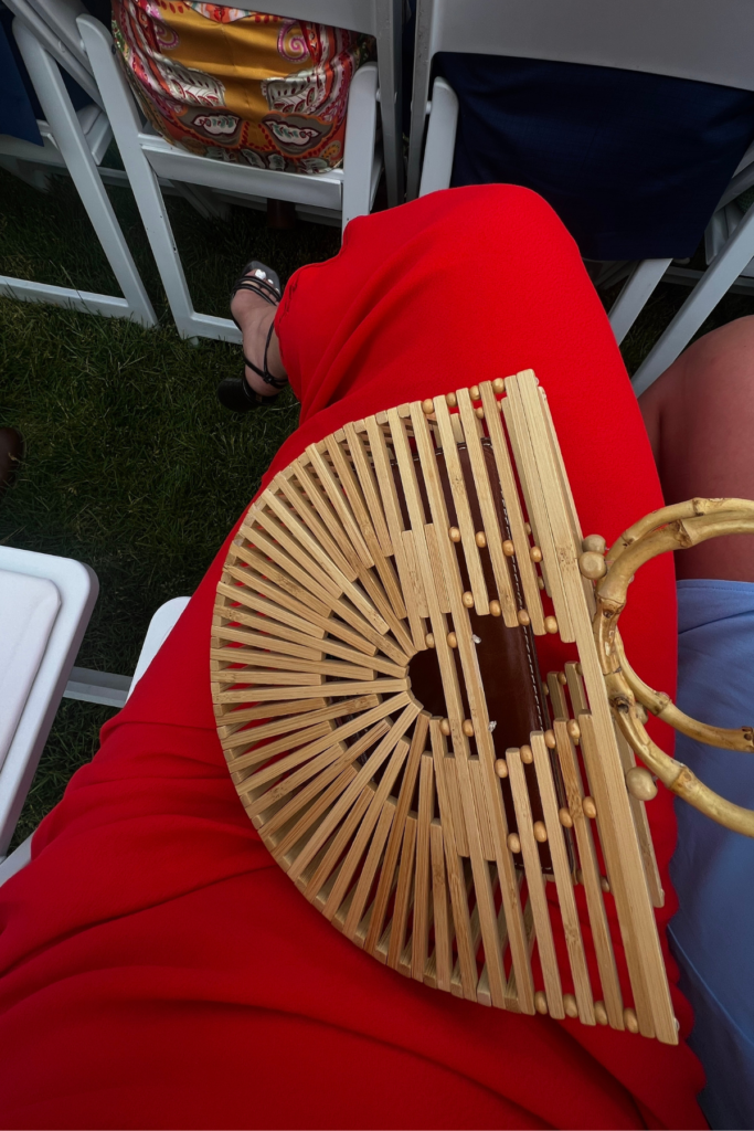 Image of red dress and wooden half circle purse on woman sitting on white chair. rent the runway honest review for wedding guest blog post.