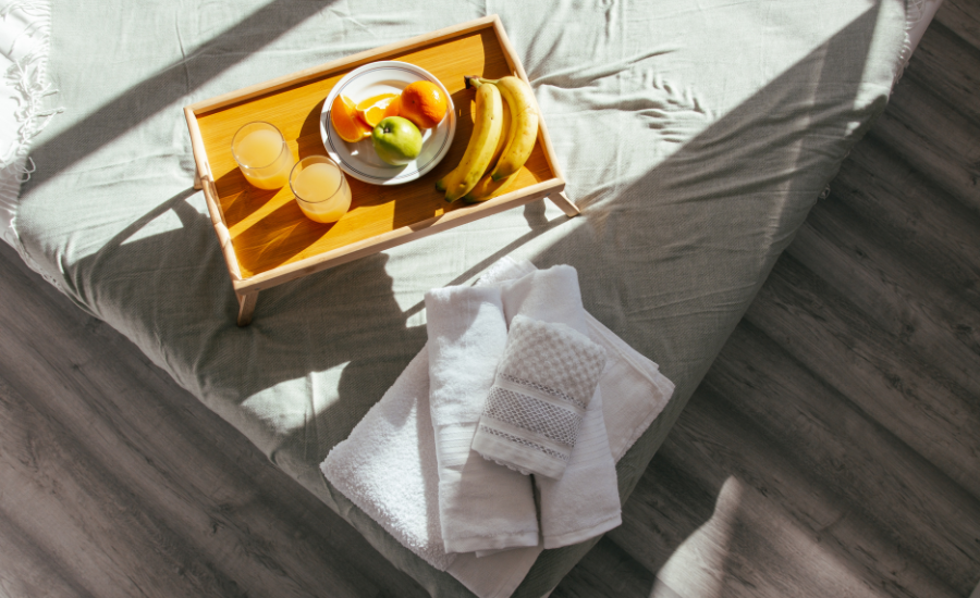 Top down image of bed corner with tray of food and folded towels in Airbnb.