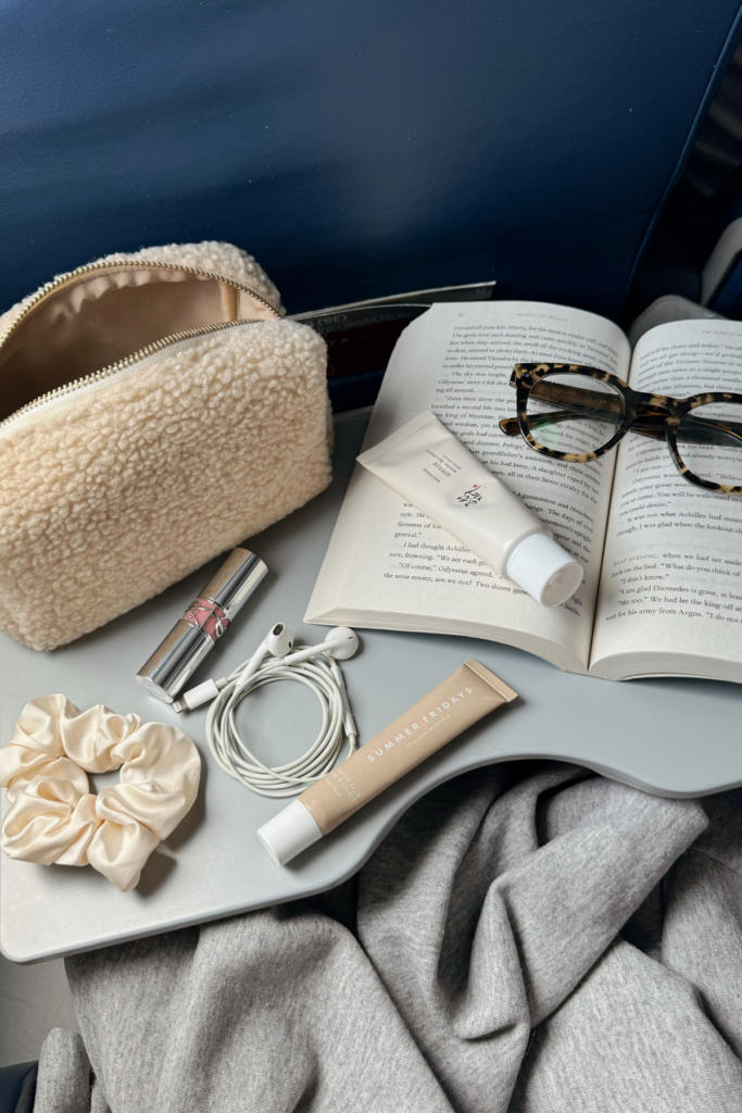 Airplane tray with book, pencil case, glasses, and makeup on top.