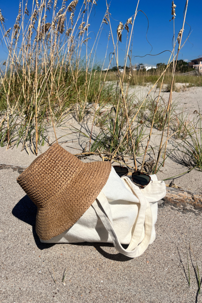 Beach hat and white cloth bag sitting on sand at beach.