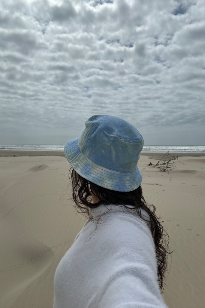 Woman in bucket hat and white sweater at the ocean.